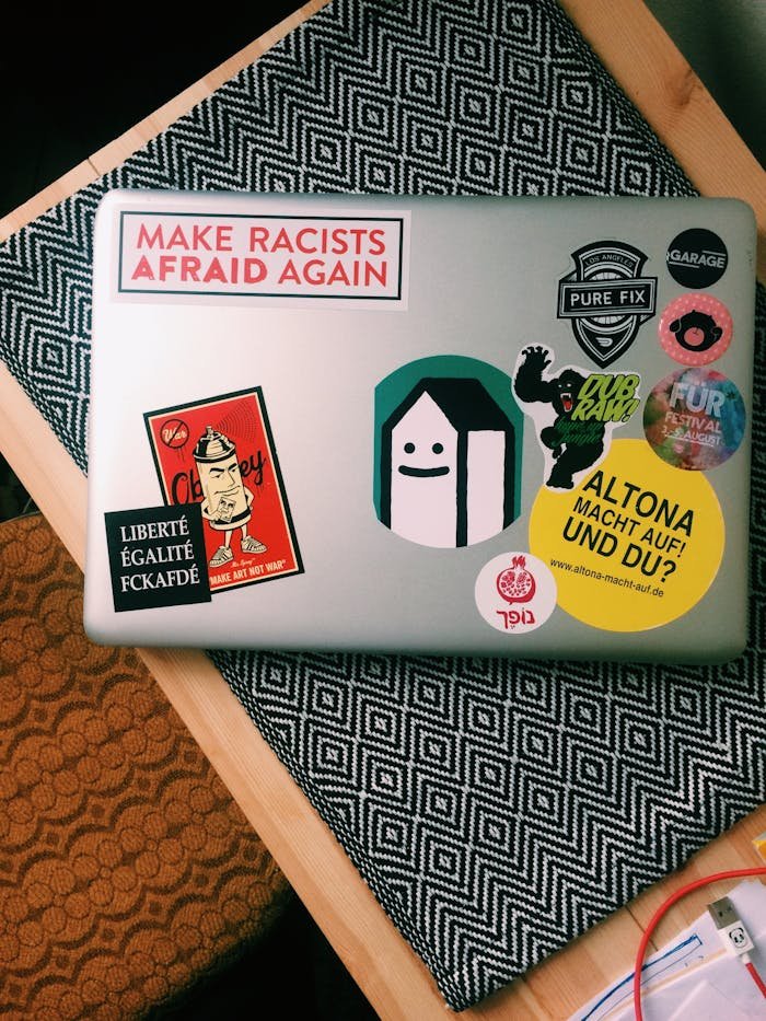 Laptop covered in colorful stickers with political and artistic themes sitting on a desk.